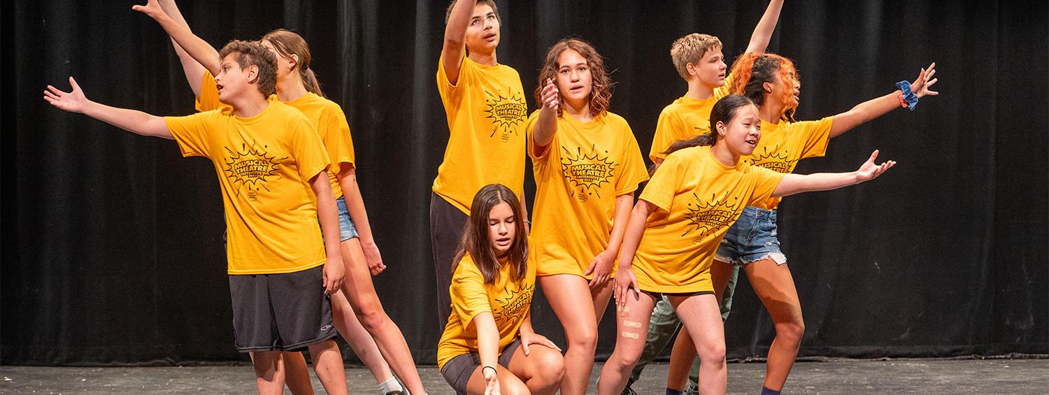 Students in yellow shirts posing with arms outstretched in summer camp class.